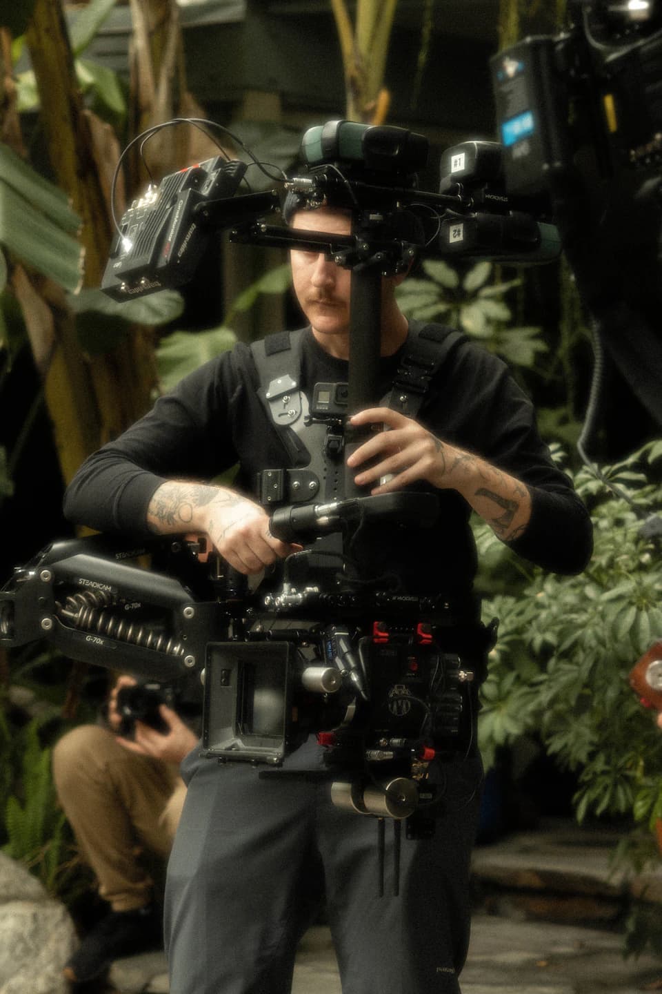 A camera operator works with a body-mounted stabilizer and cinema camera outdoors.