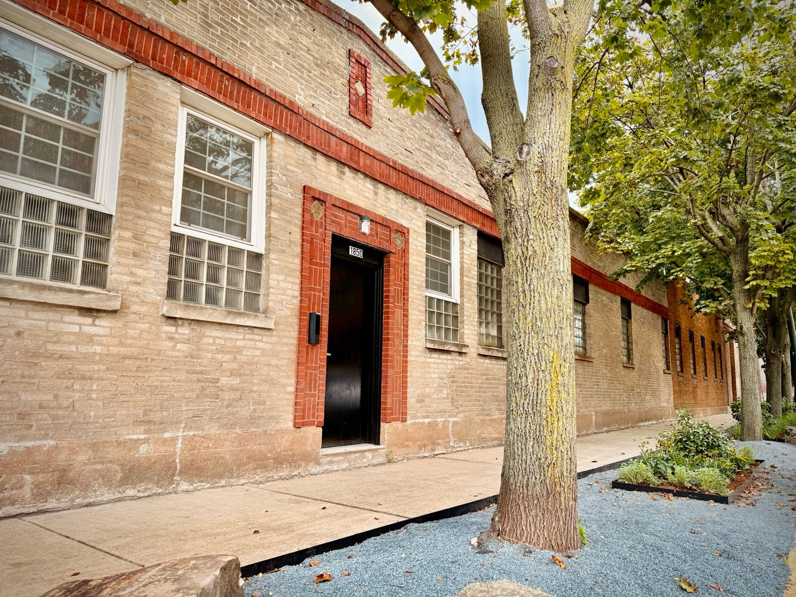 Street entrance of the Bada Office, a brick building with red trim and a black door under a row of trees