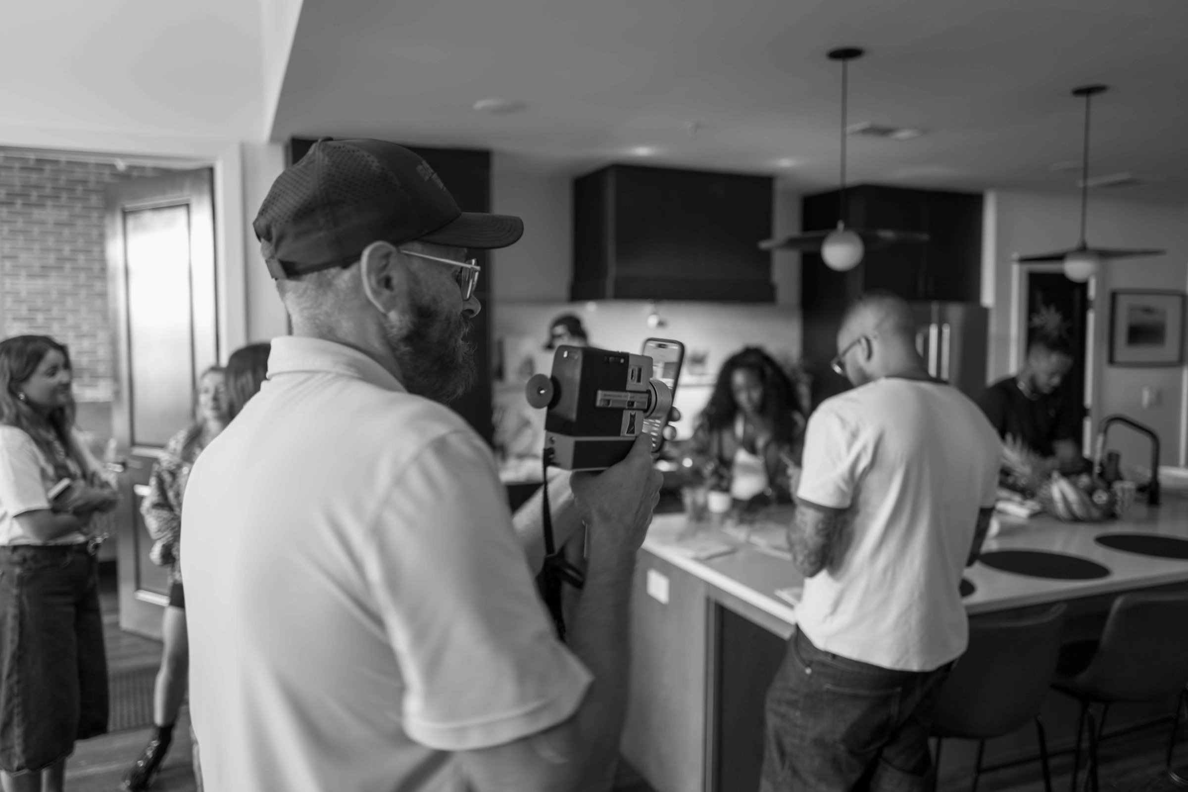 Director checking a handheld monitor while talent and crew work around a kitchen island on a location shoot