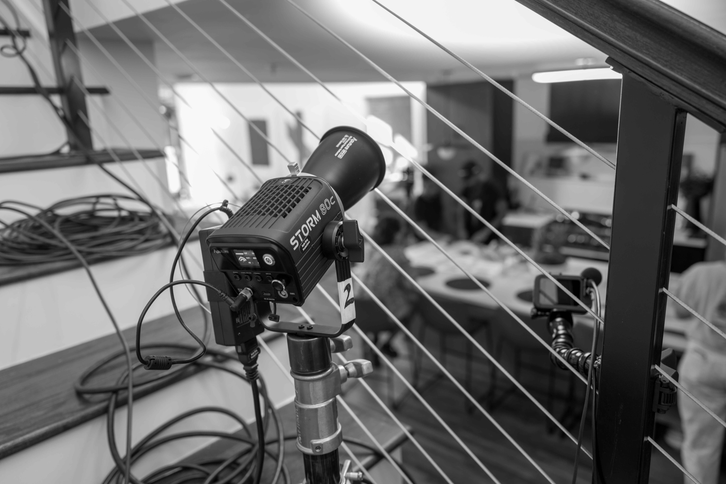An Aputure Storm 80c light on a stand with cables coiled, set up on a staircase overlooking a location shoot