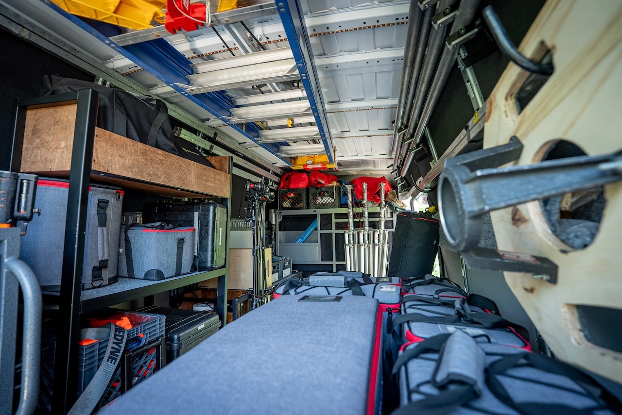 Inside the 2 ton grip truck looking down the standing-height cargo bay past shelved gear toward the cab
