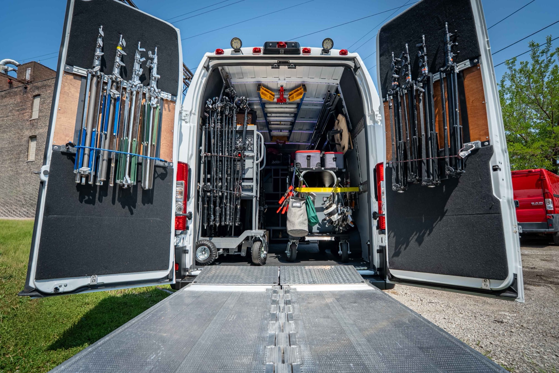 Rear of the 2 ton Ram ProMaster 3500 grip truck with both doors open and the Tommy Gate liftgate lowered, loaded with C-stands, light stands and cases